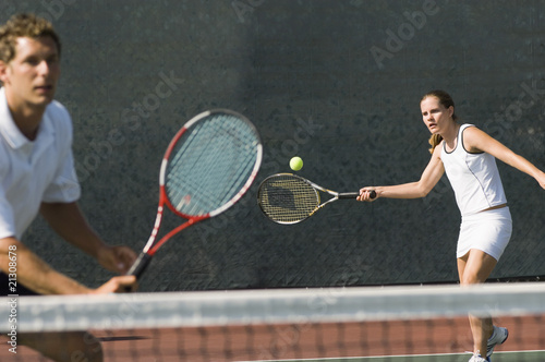 mixed doubles player hitting tennis ball partner standing near net