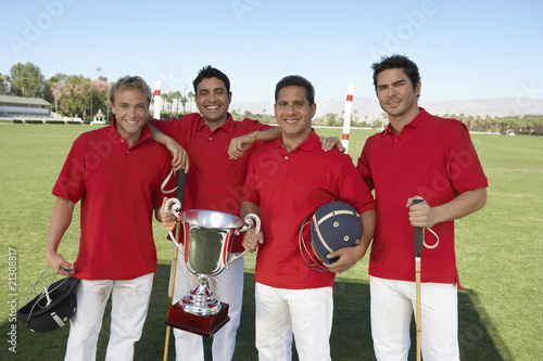 smiling polo players standing on polo field holding equipment and trophy