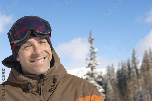 young man wearing ski goggles on head in snow portrait.