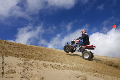 Male riding ATV up sand dune hill