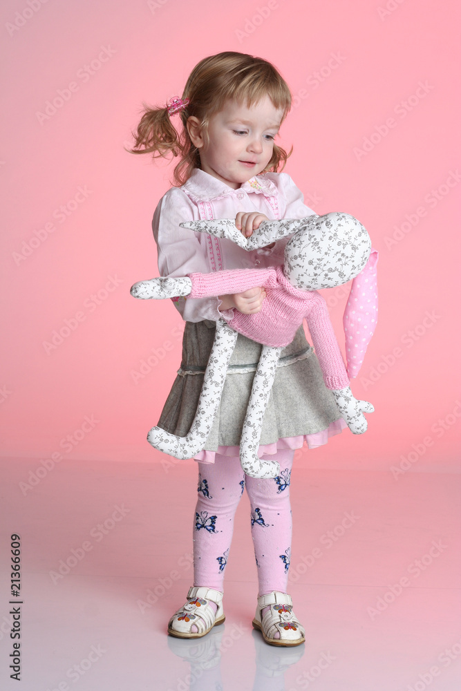 Little girl is playing with rabbit toy in studio on pink Little girl is playing with rabbit toy in studio on pink