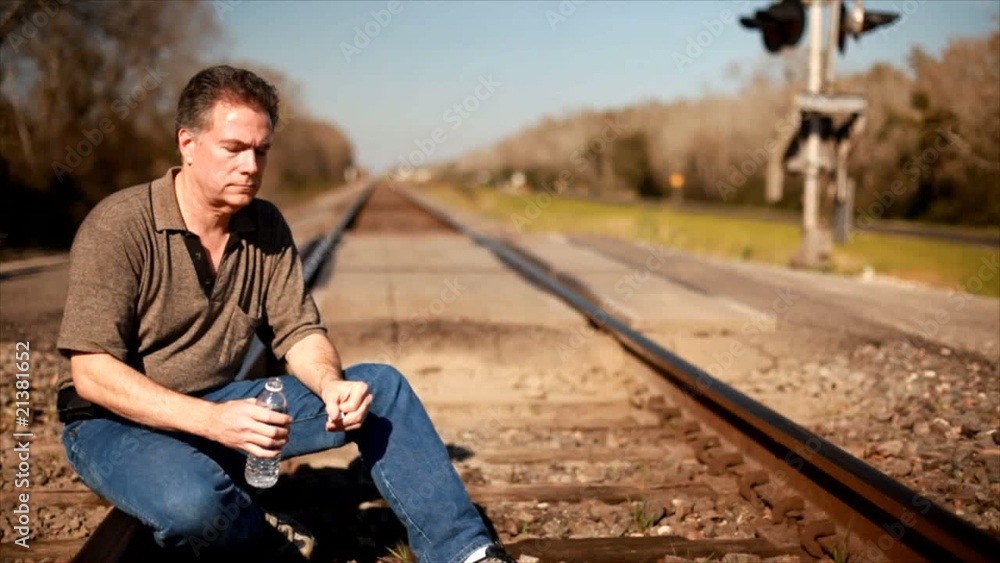 A man sitting on a railroad track drinking some water. A man sitting on a railroad track drinking some water.