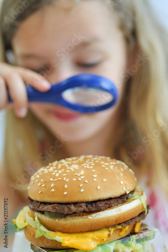 Fillette examinant un hamburger avec une loupe. photo