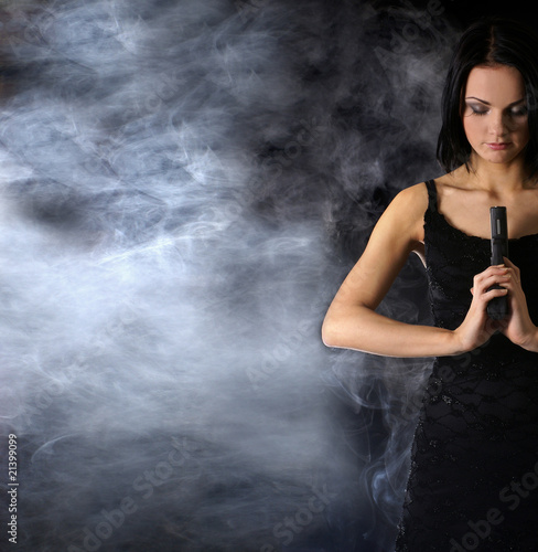 Attractively looking woman with a gun on a smoky background