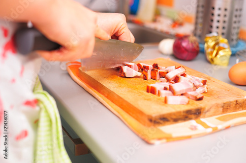 Girl in apron cutting meat on wooden cutting board