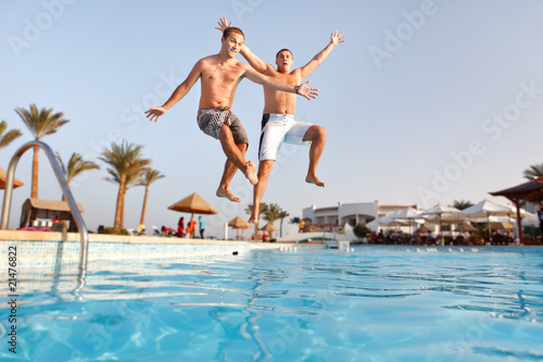 Two men jumping in swimming pool together