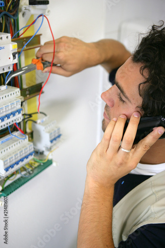 portrait d'un éléctricien au téléphone devant un disjoncteur
