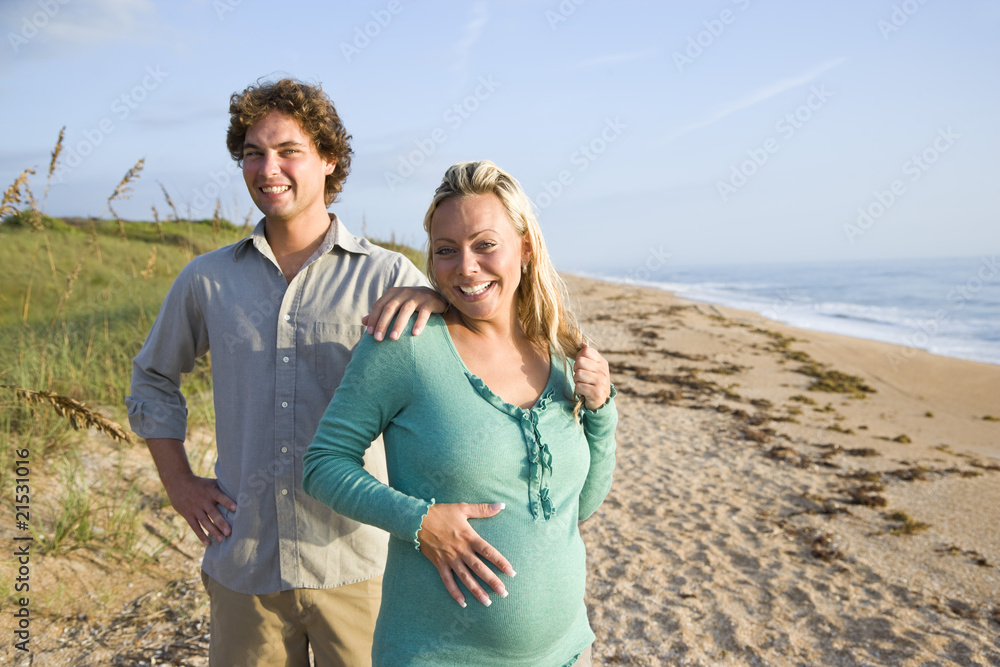 Happy young pregnant couple standing together at beach Happy young pregnant couple standing together at beach