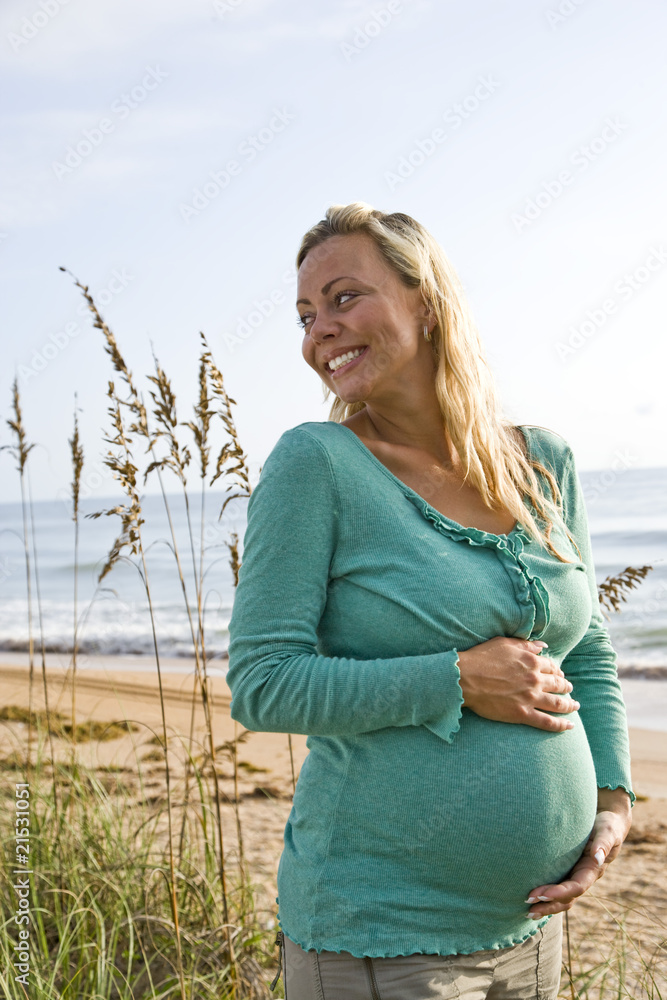 Happy young pregnant woman standing outdoors alone at beach Happy young pregnant woman standing outdoors alone at beach