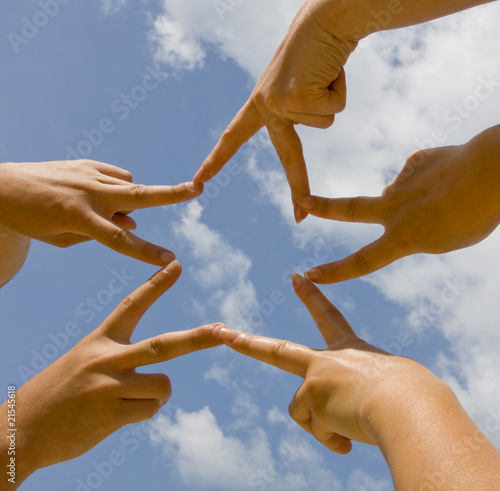 Many hands connecting to star shape under sky