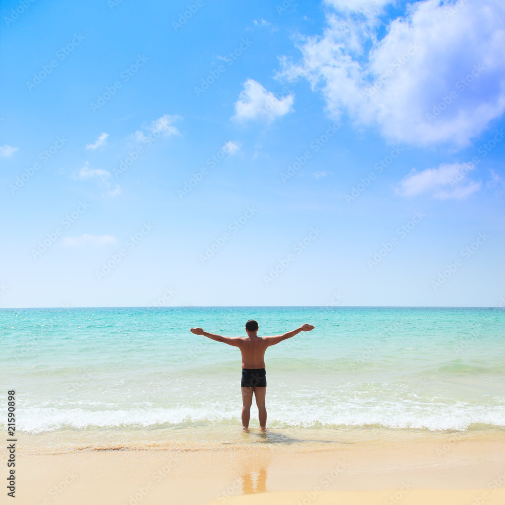 relaxed young man with his hands stretched, standing at the beac