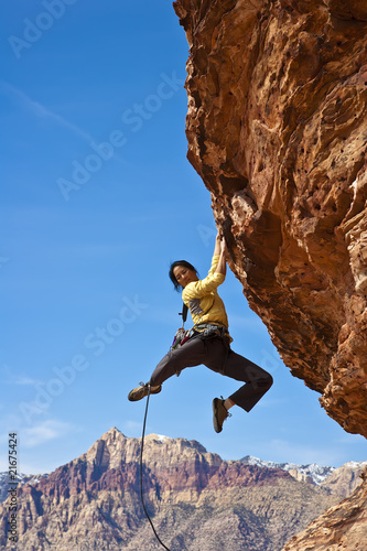 Female rock climber reaching for the summit.