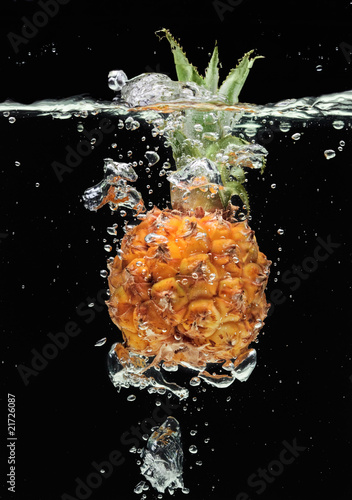 Small pineapple falling in water on black