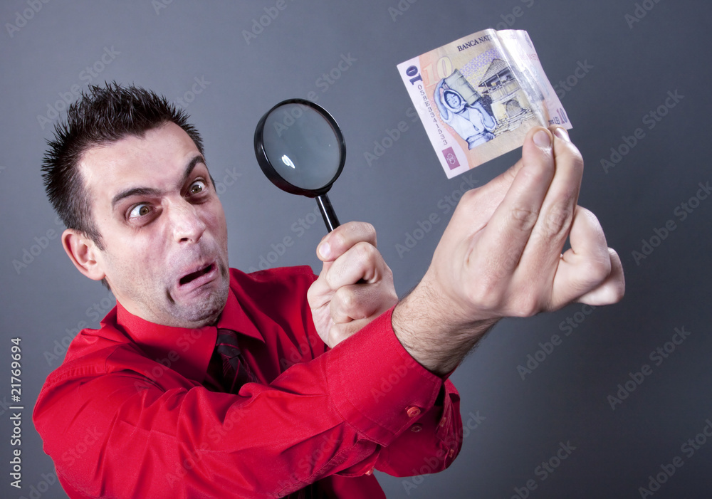 Funny businessman looking at banknote with magnifying glass Funny businessman looking at banknote with magnifying glass
