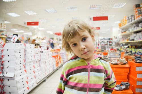 little girl in supermarket alone, chooses in department footwear