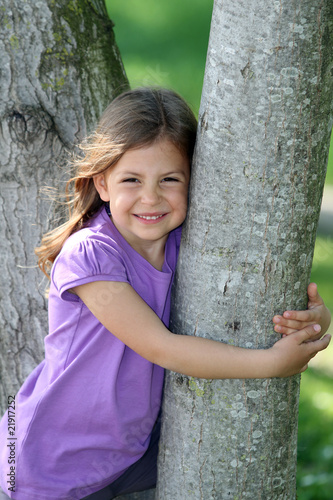 Cute young girl smiling and hugging a tree © wazymodo