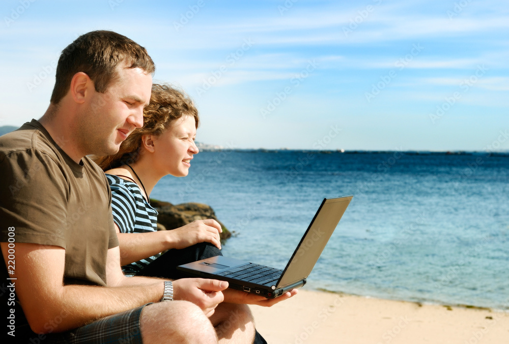 man and woman with computer at beach