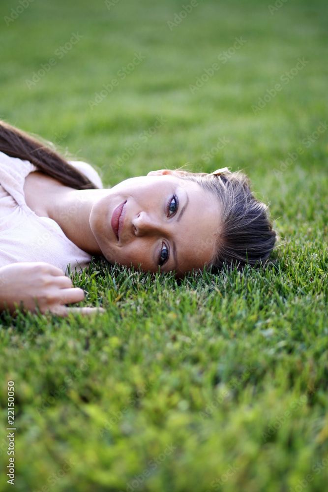 Cute young female lying on grass field at the park .