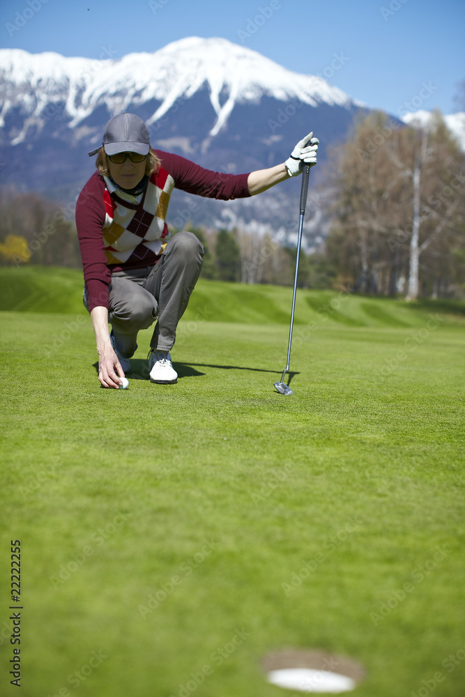 Woman golfer aligning golf ball to a hole on a putting green