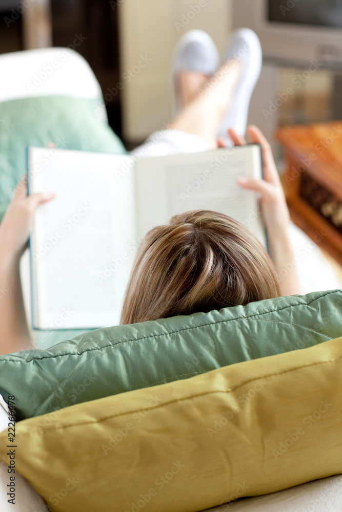 Blond woman reading a book lying on a sofa Blond woman reading a book lying on a sofa