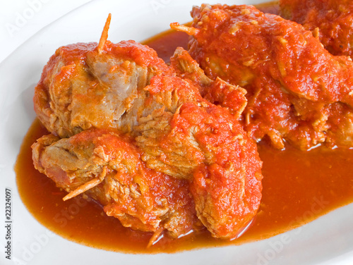 Meat roulade in tomato sauce on white dish.