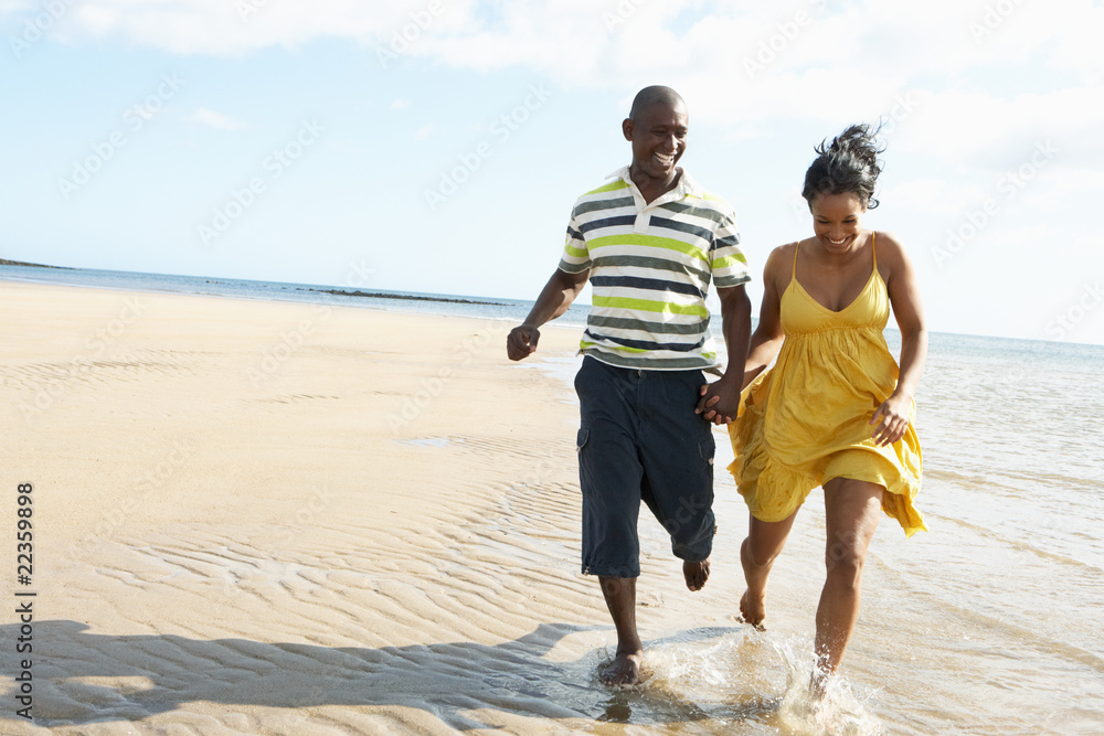 Romantic Young Couple Running Along Shoreline Of Beach Holding H