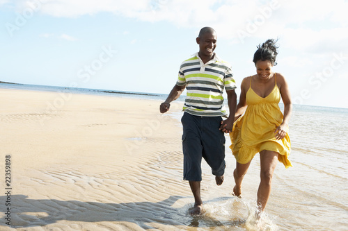 Romantic Young Couple Running Along Shoreline Of Beach Holding H