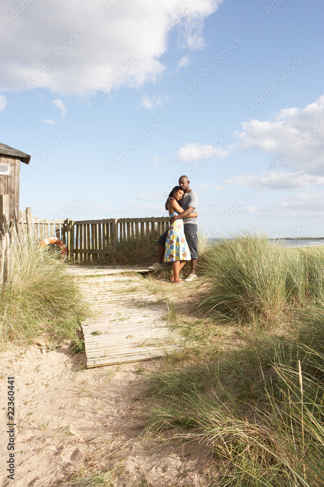 Romantic Young Couple Standing By Wooden Fence Of Beach Hut Amon