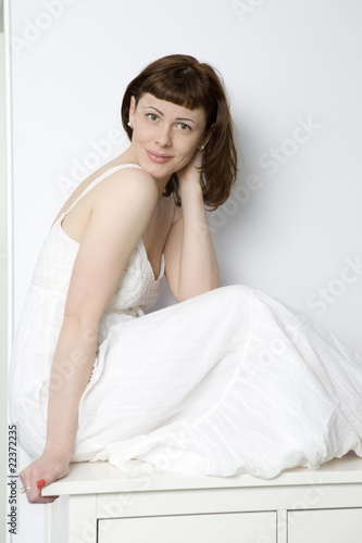 flirting woman in white dress sitting on chest of drawers