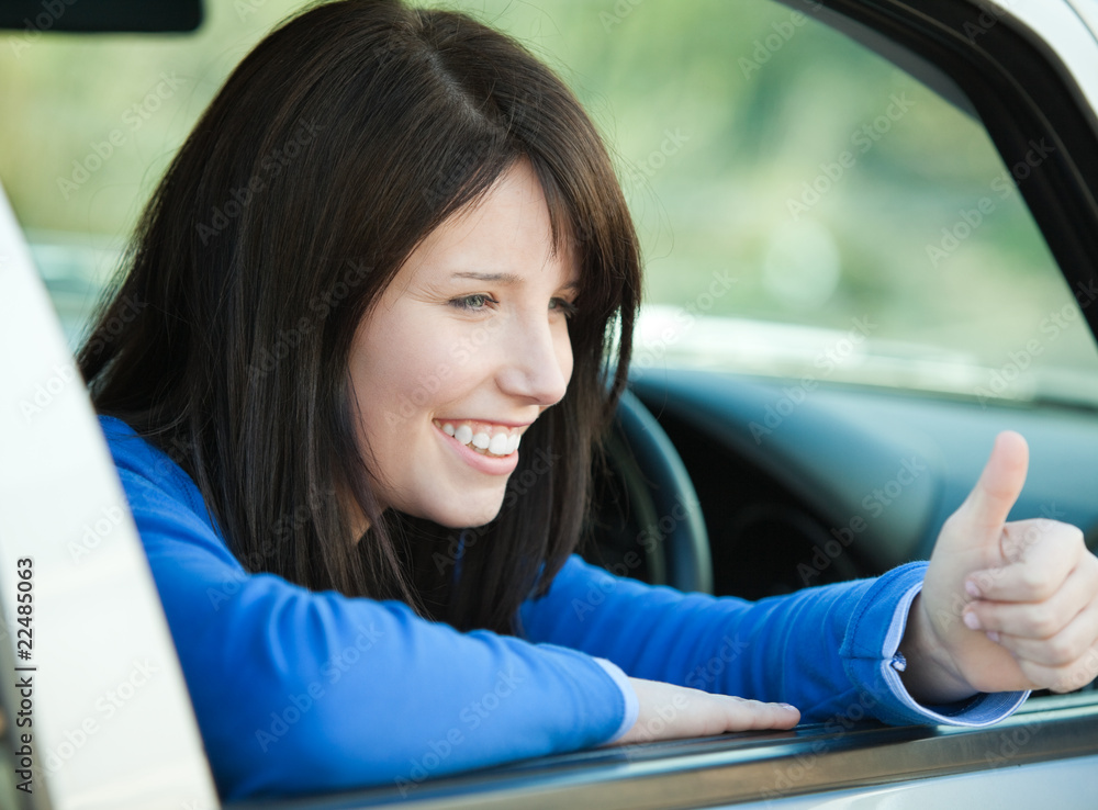 Smiling teen girl with a thumb up sitting in her car