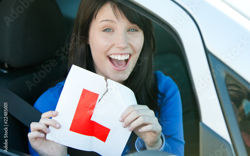 Happy brunette teen girl sitting in her car tearing a L-sign photo