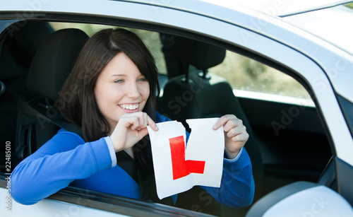 Joyful teen girl sitting in her car tearing a L-sign photo