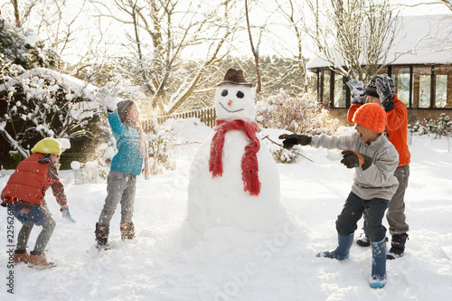Mother And Children Building Snowman In Garden