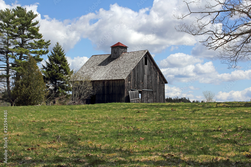 Obraz premium Old worn barn in field with bright cloudy sky