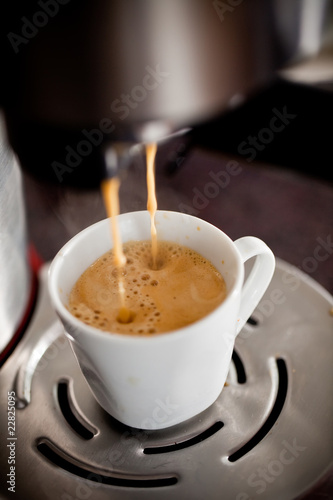 Coffee maker pouring hot espresso coffee in a cup