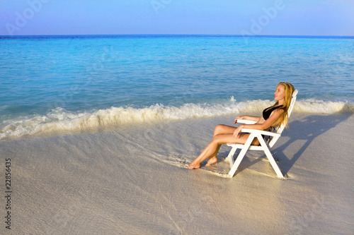 Young pretty woman tans in beach chair  in ocean photo