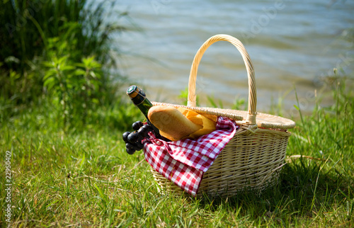Picnic basket with food and cider bottle near the water