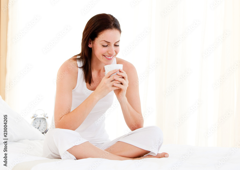 Smiling woman drinking a coffee sitting on her bed