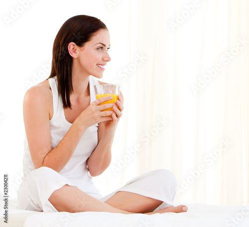 Cheerful woman drinking an orange juice sitting on her bed