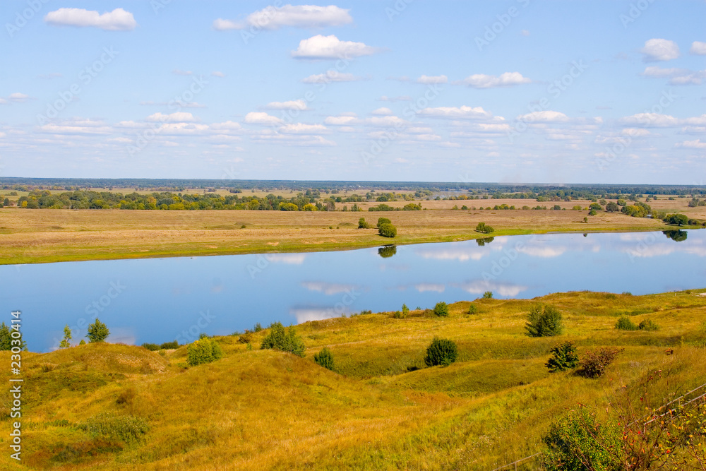 Beautiful river and yellow meadow under the summer sky
