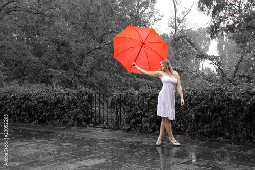 Eine sehr weibliche Frau im Sommerkleid bei grauem Regenwetter mit rotem Schirm photo