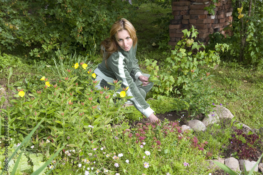 Young pretty woman looks after behind plants in the garden Young pretty woman looks after behind plants in the garden