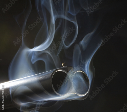 Both barrels of a double barrel shotgun oozing smoke after a shot on a dark background