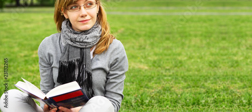 The girl sits on a grass, reads the book