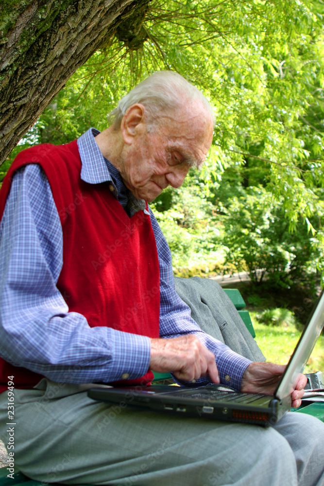 Alter Mann arbeitet mit dem Laptop im Grünen Alter Mann arbeitet mit dem Laptop im Grünen