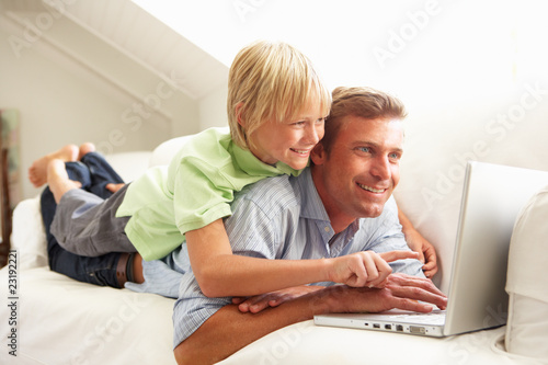 Father And Son Using Laptop Relaxing Sitting On Sofa At Home