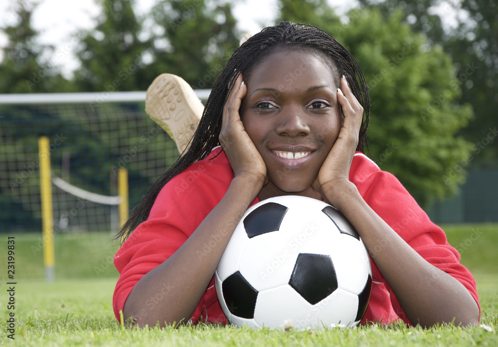 Obraz premium Junge Afrikanerin mit Fussball vor dem Tor liegend