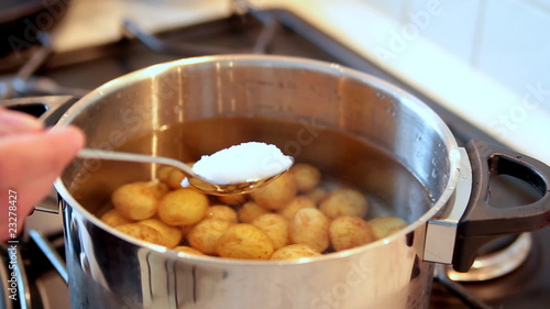 Potatoes in pot and hand with spoon adding salt