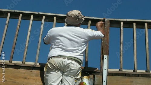 PINTOR BARNIZANDO UNA BARANDILLA DE MADERA DE UN PUENTE