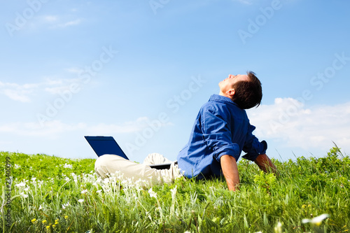 Man working with laptop in a meadow of flowers with copyspace